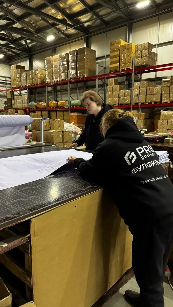 Сотрудницы склада Prime Partner раскраивают белую ткань на столе нарезки